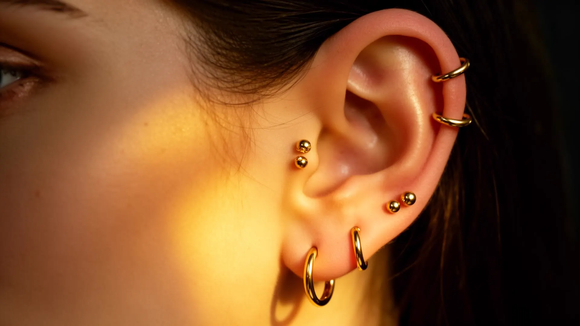 Editorial close-up of gold piercings on the ear — Eternal Tattoo & Piercing
